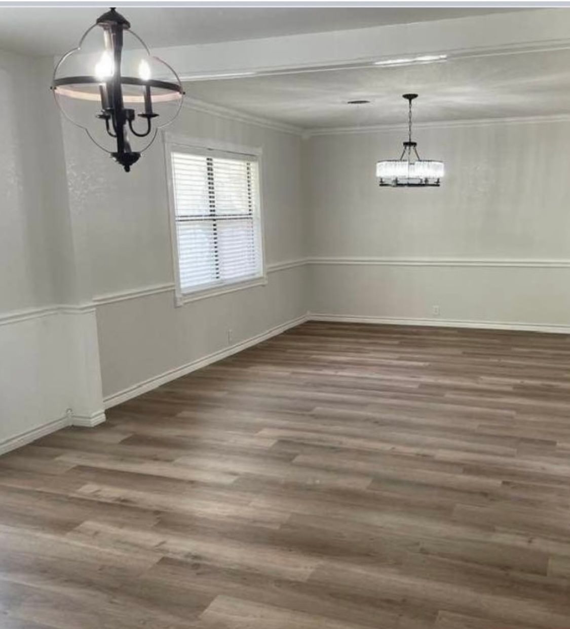 An empty dining room with hardwood floors and a chandelier hanging from the ceiling.
