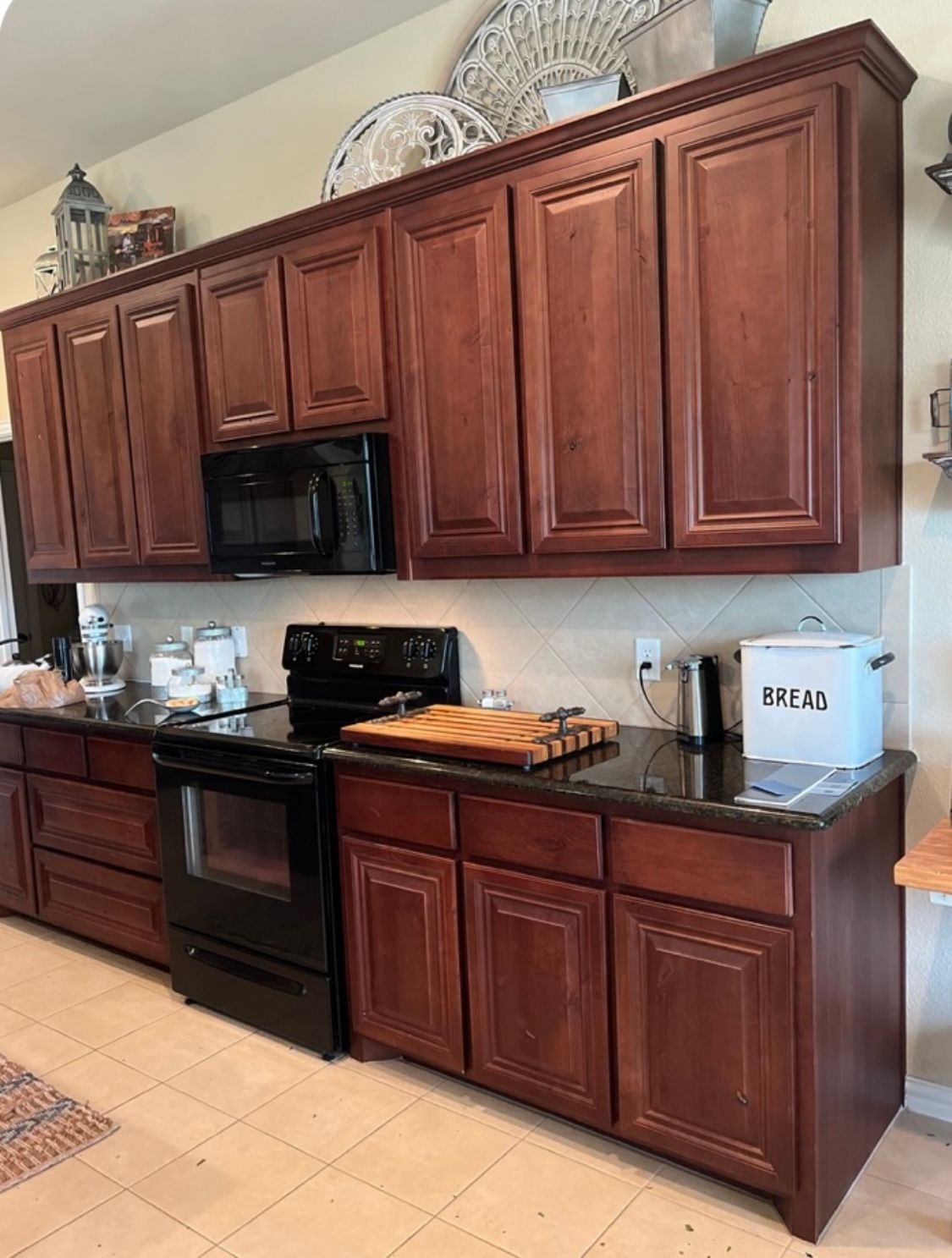 A Kitchen with Wooden Cabinets , a Black Stove , a Microwave , and A Cutting Board.