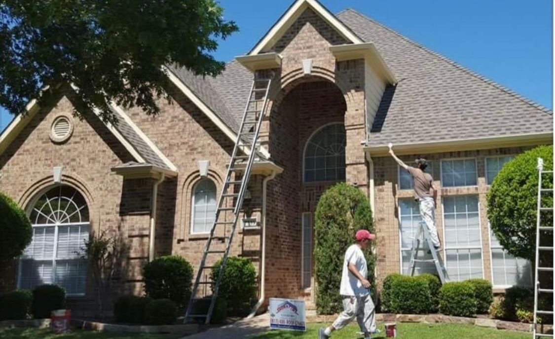 Two men are painting a brick house with a ladder.