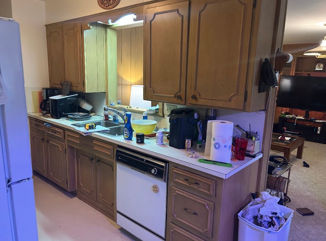 A kitchen with wooden cabinets , a dishwasher , a refrigerator and a trash can.
