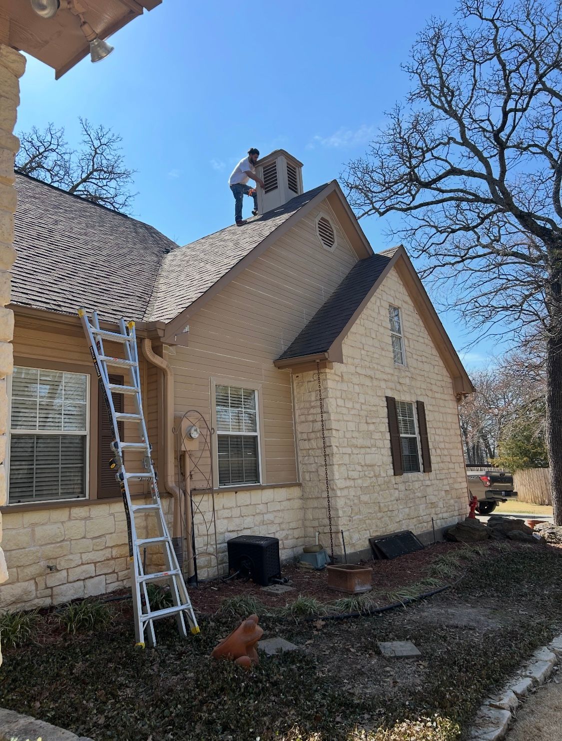 A man is standing on the roof of a house with a ladder.