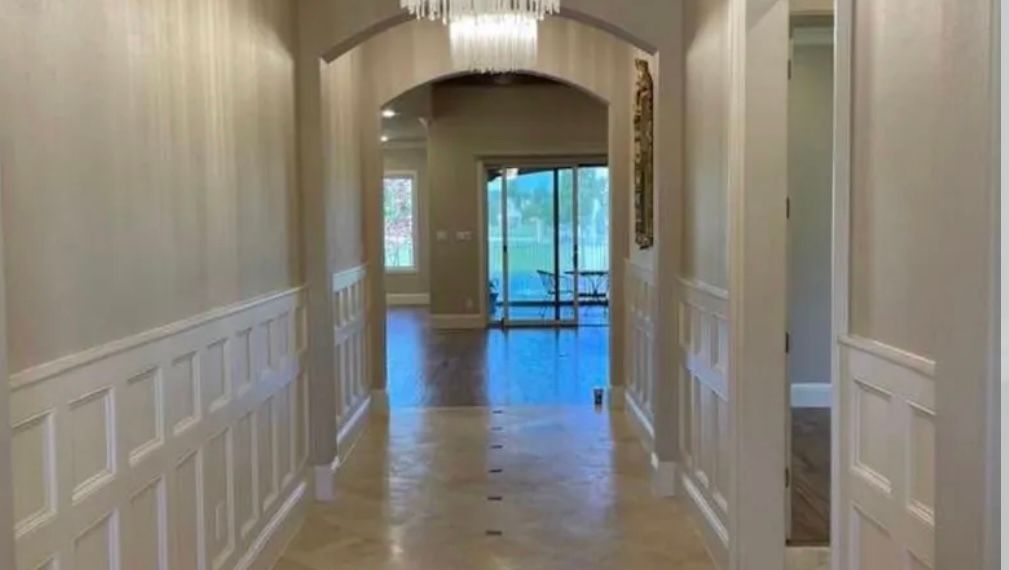 Hallway with wainscoting and archway leading to a bright outdoor view, featuring a chandelier.