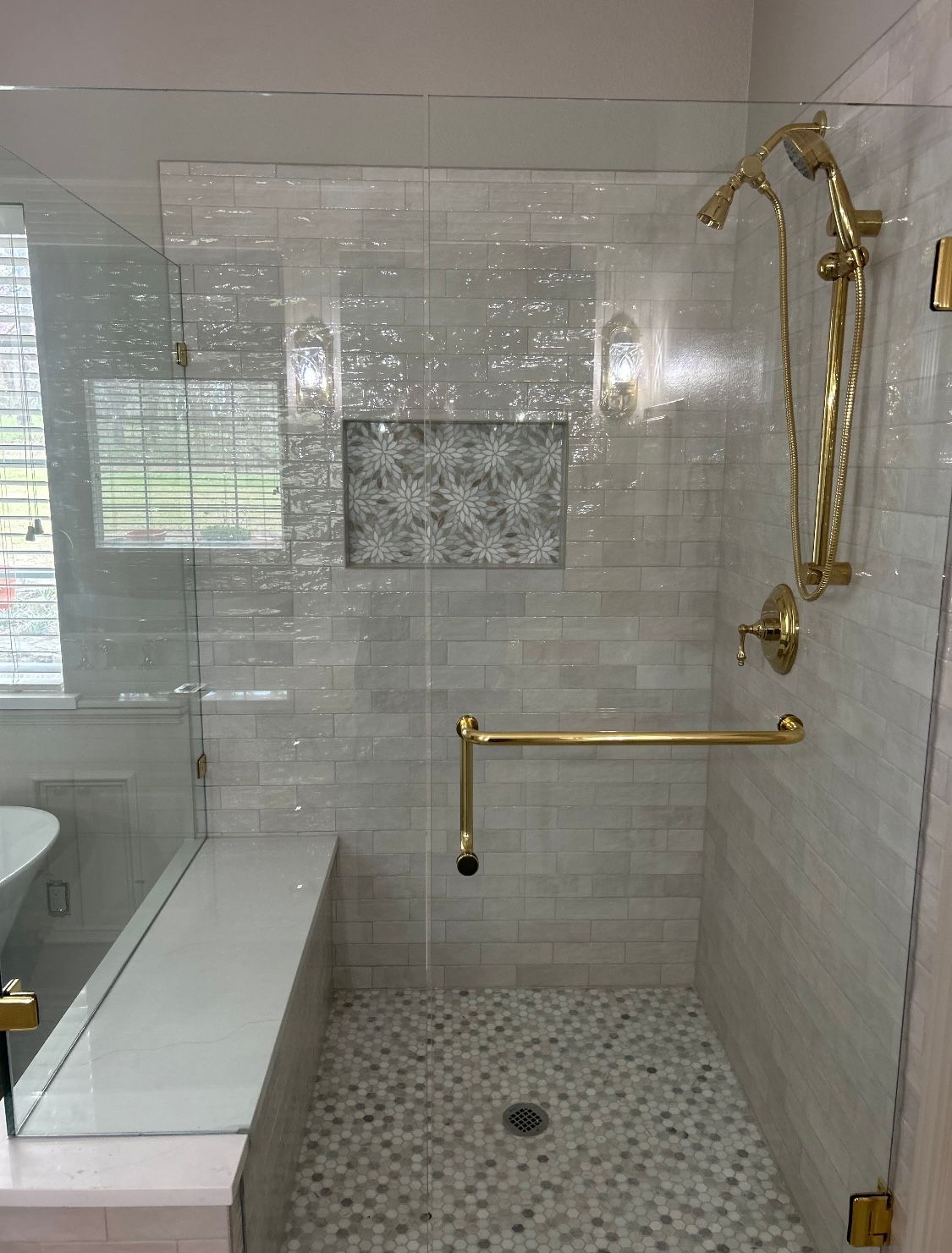 Modern bathroom with gold fixtures and white tile shower; includes a built-in bench and grab bar for accessibility.