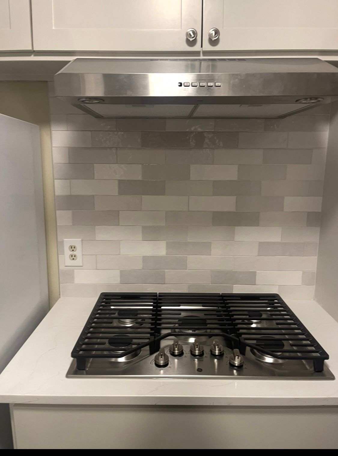 Gas stovetop with stainless steel hood and white tile backsplash in a kitchen.