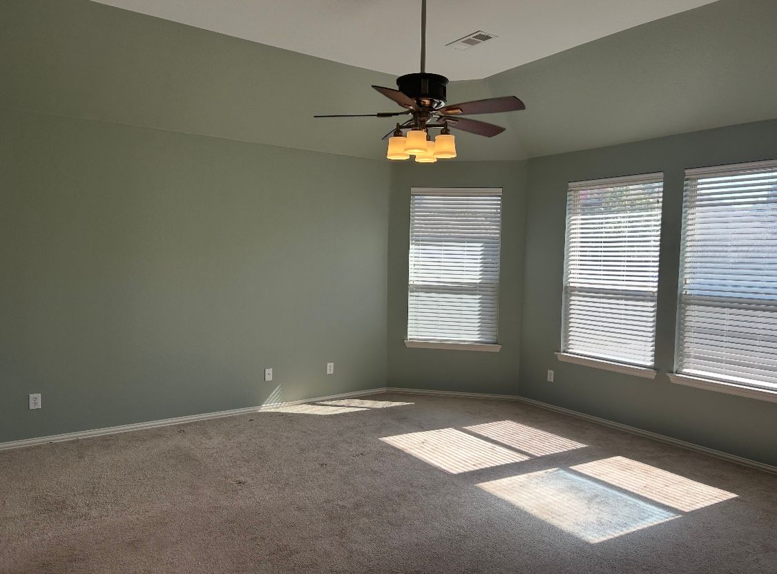 An empty living room with a ceiling fan and blinds.