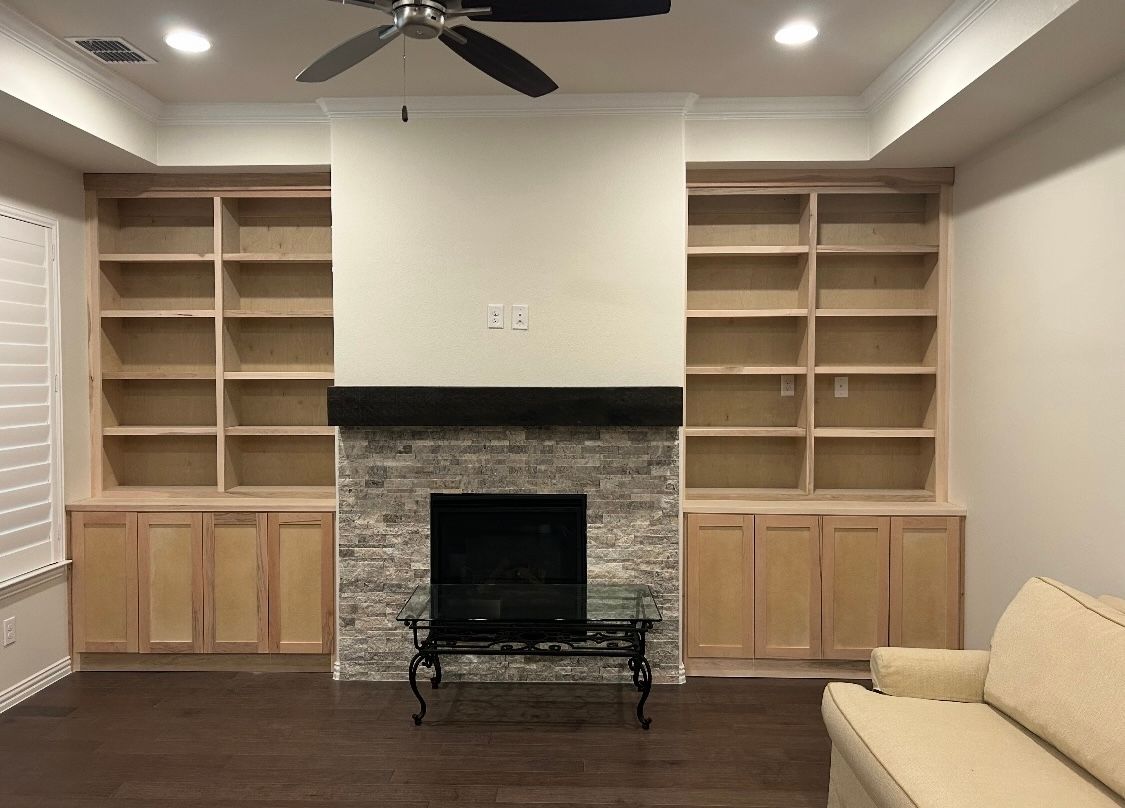 A living room with a fireplace , couch , shelves and a ceiling fan.