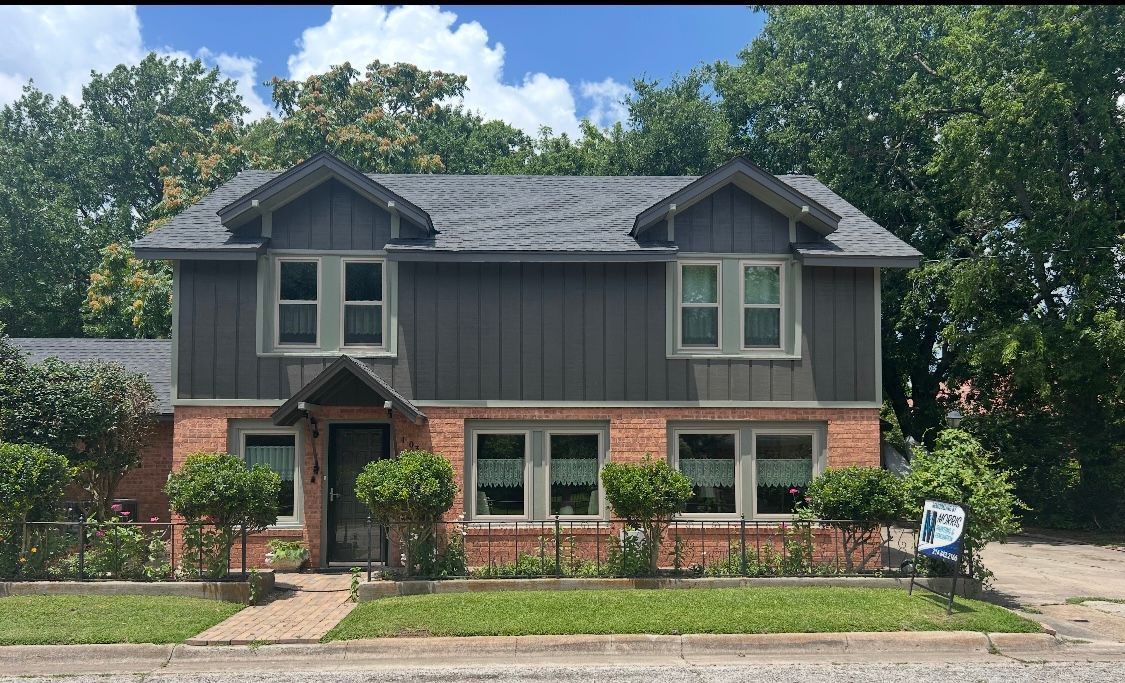 A large brick house with a gray siding and a gray roof is for sale.