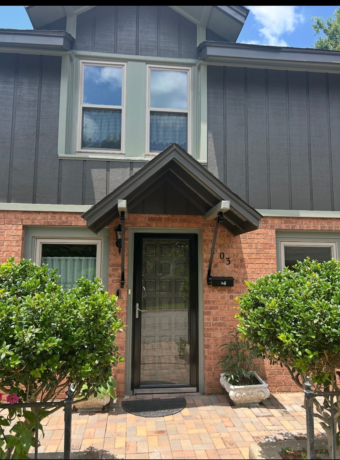 A brick house with a gray siding and a black door