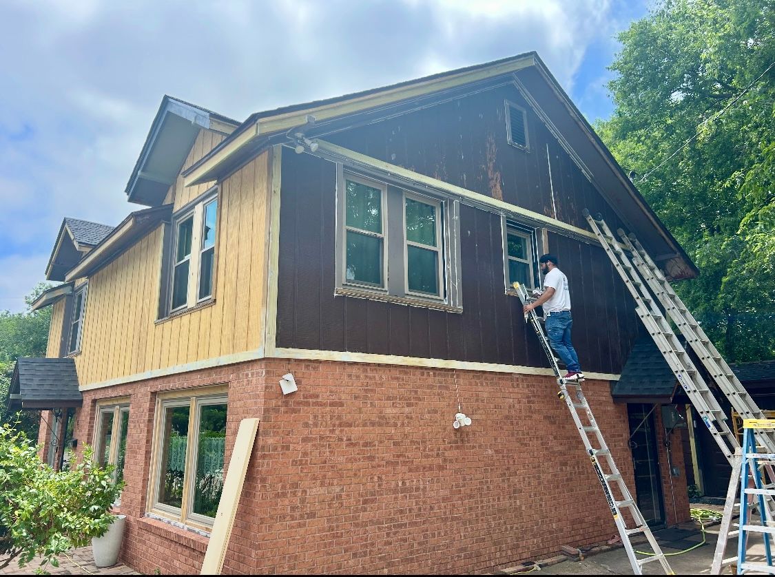 A man is standing on a ladder on the side of a house.