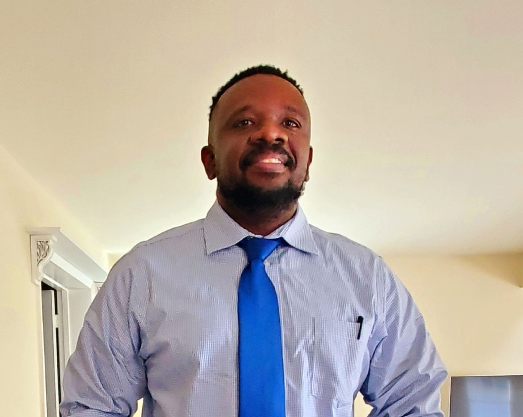 A man in a blue shirt and blue tie is smiling for the camera