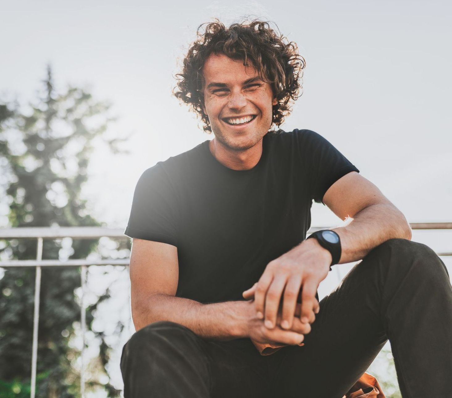 A man in a black shirt is sitting on a railing and smiling