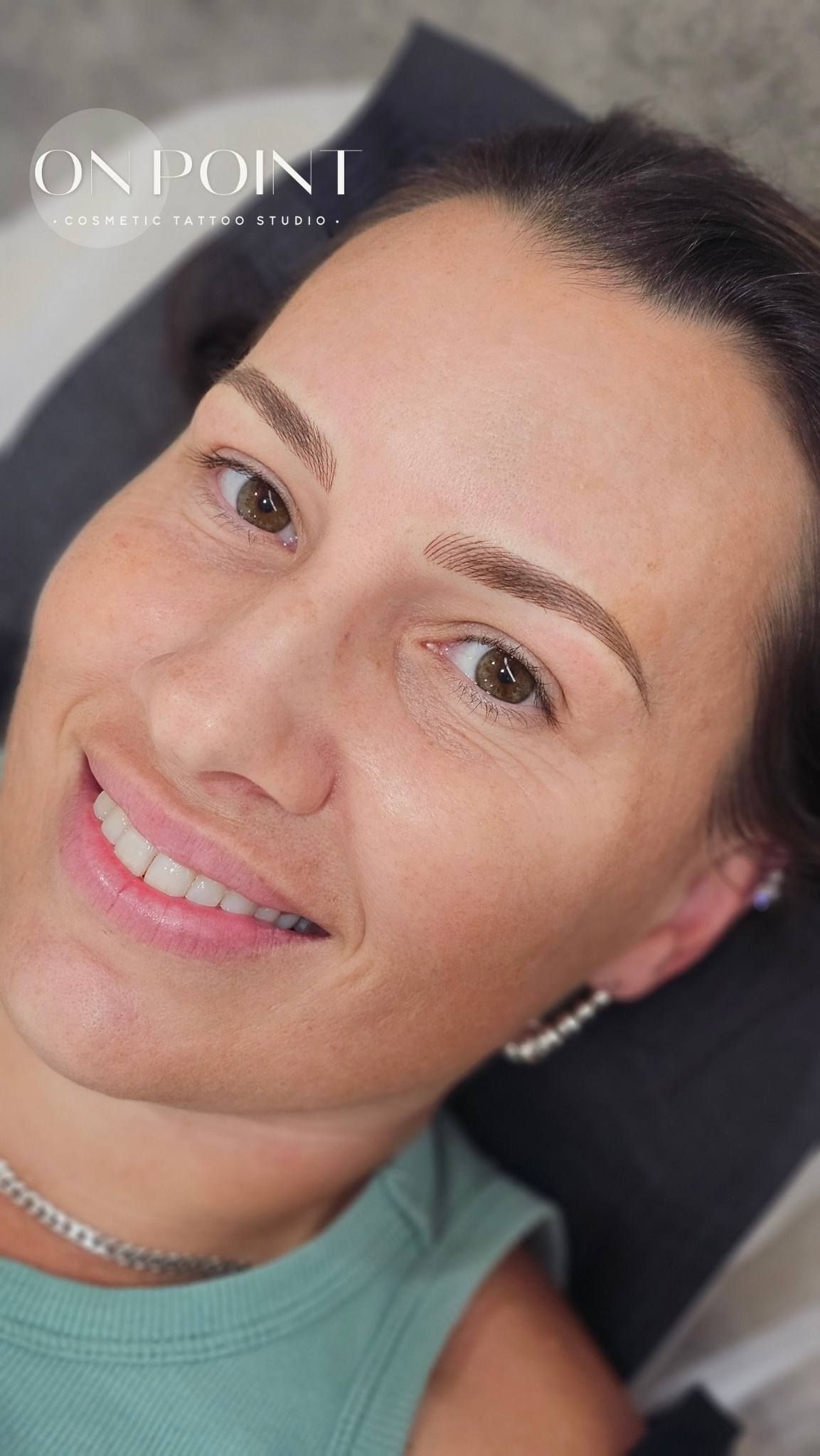 Woman with newly tattooed eyebrows smiles. Light brown brows, neutral background.