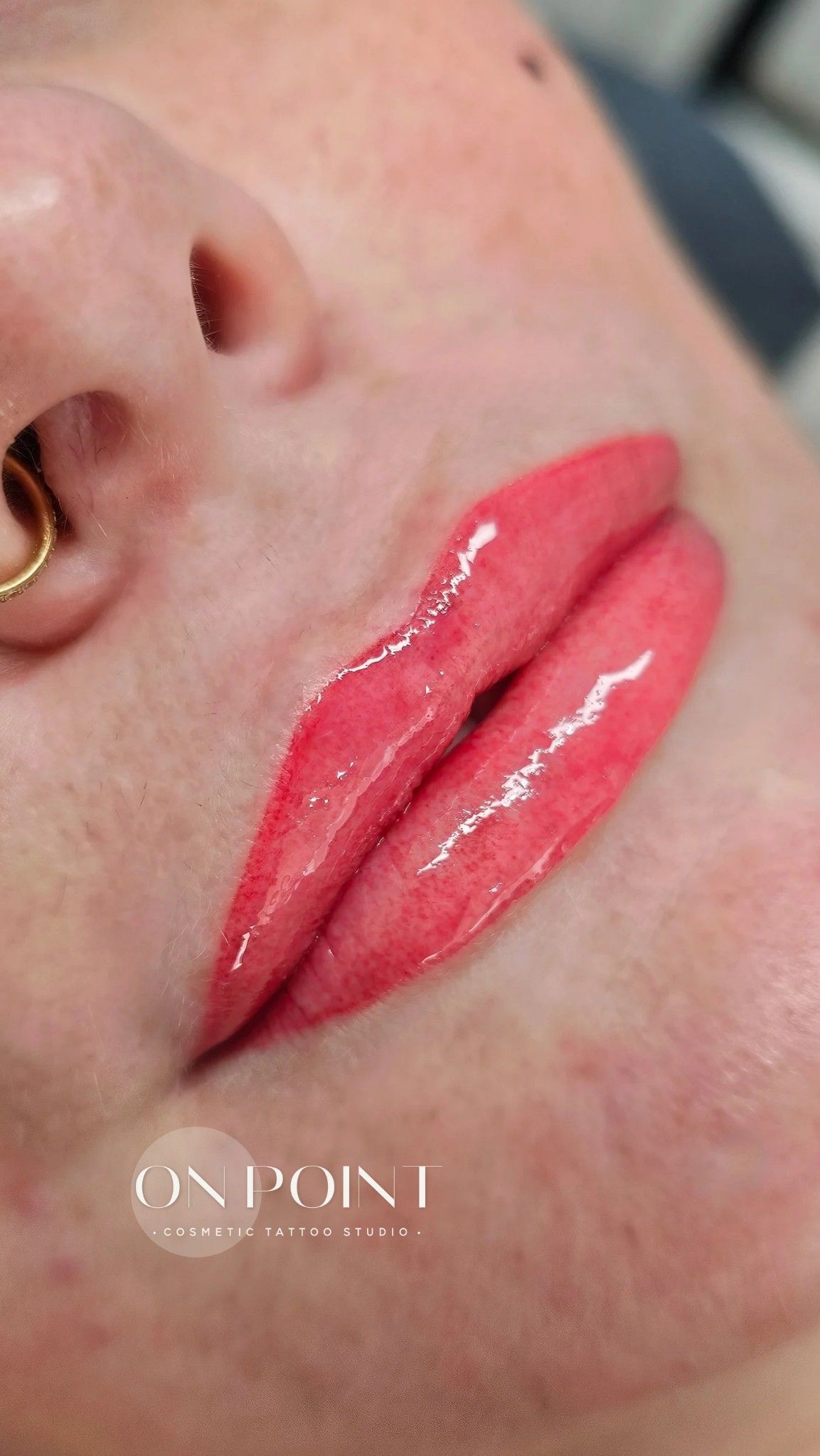 Close-up of freshly tattooed lips in a vibrant coral color; part of a face with a nose ring.
