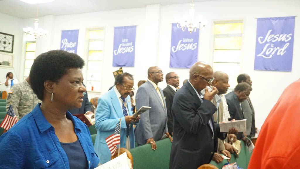 A group of people are standing in a church with jesus lord banners on the walls.