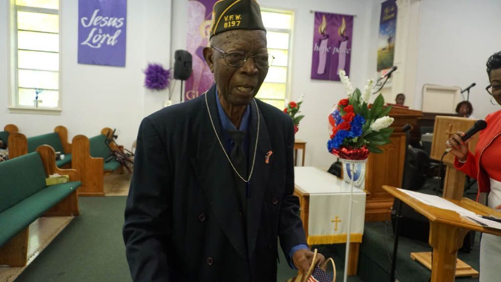 A man in a suit and hat is standing in a church holding an american flag.