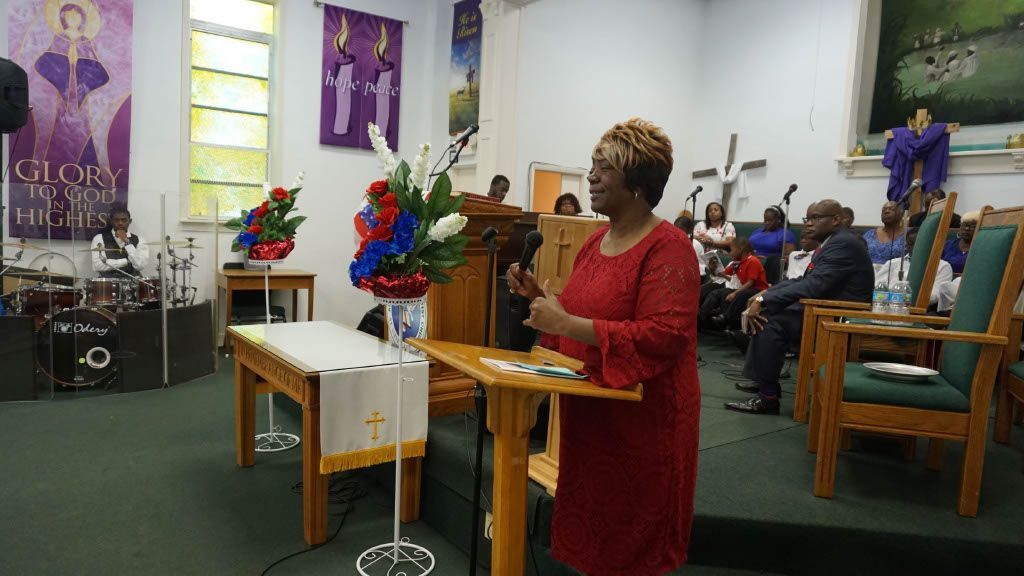 A woman in a red dress is standing at a podium giving a speech in a church.