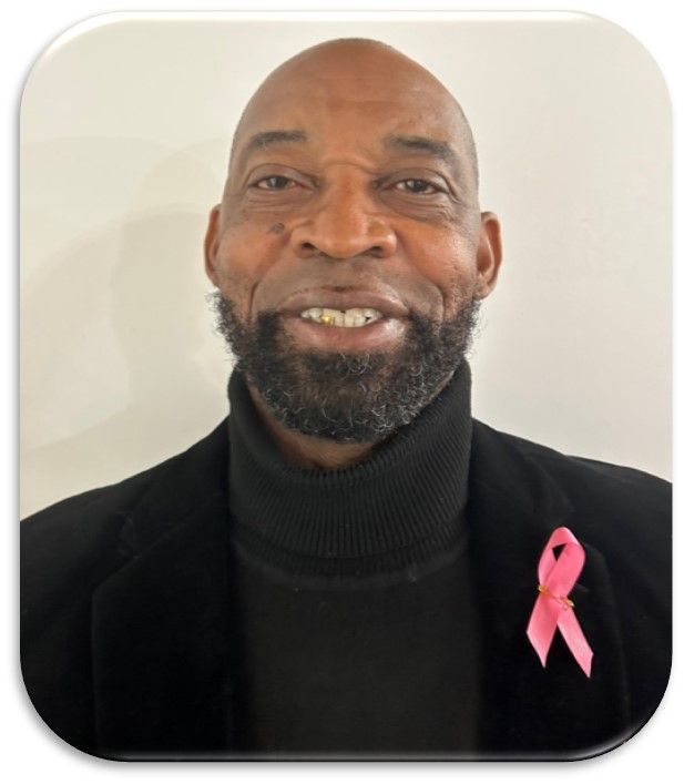 A man wearing a black turtleneck and a pink ribbon on his jacket