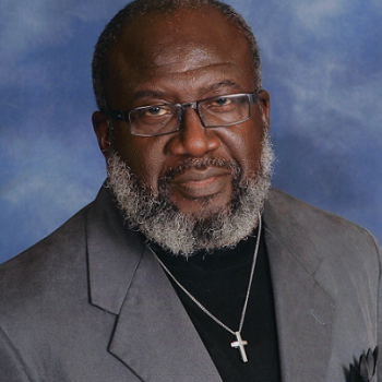 A man with a beard wearing glasses and a cross necklace