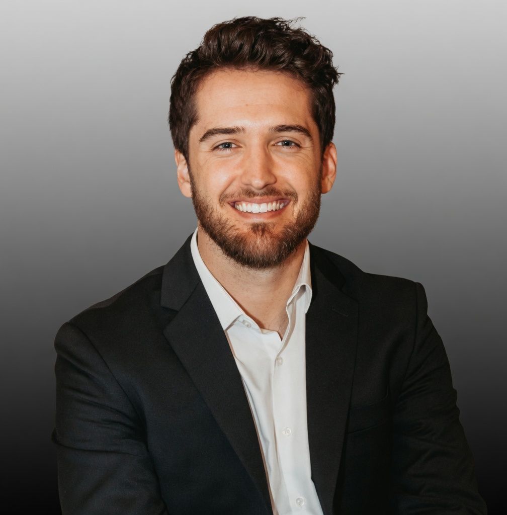 Smiling man in a black blazer and white shirt against a gray background