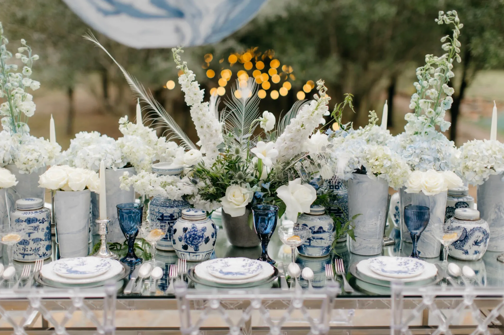 A long table with plates , glasses , vases and flowers on it.