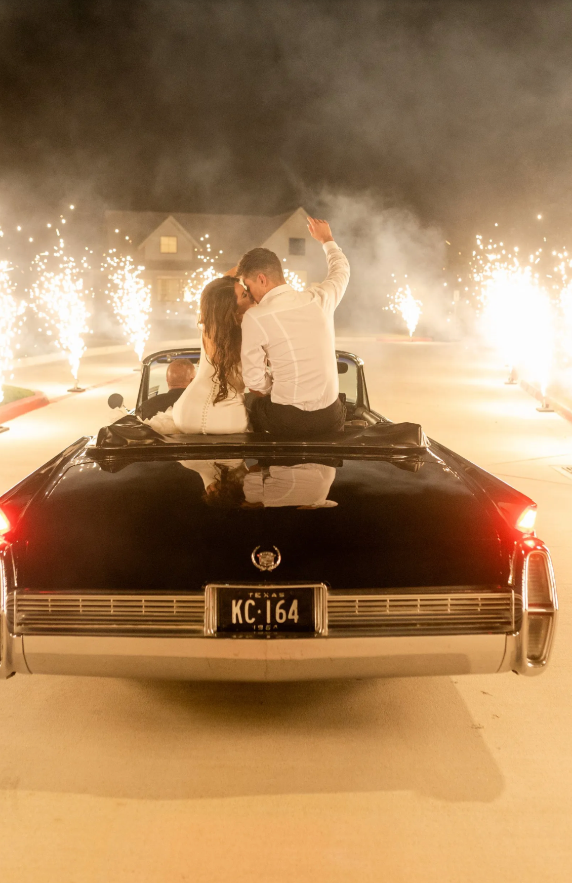 A bride and groom are sitting in the back of a convertible car.