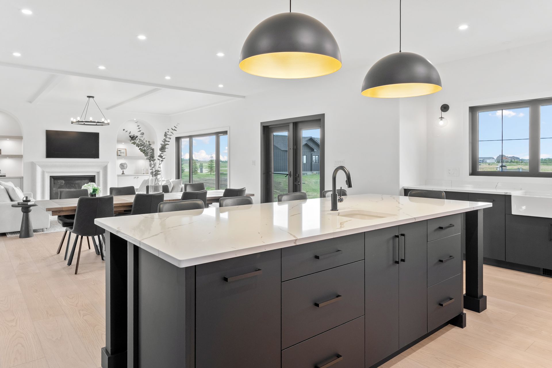 Modern kitchen with large island, dark cabinets, pendant lights, and bright open living area