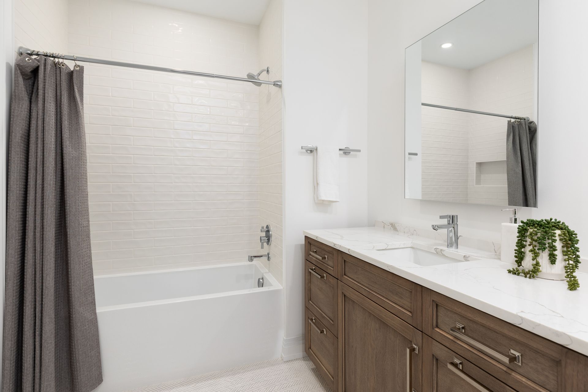 Modern bathroom with white tub, gray curtain, and wood vanity with mirror