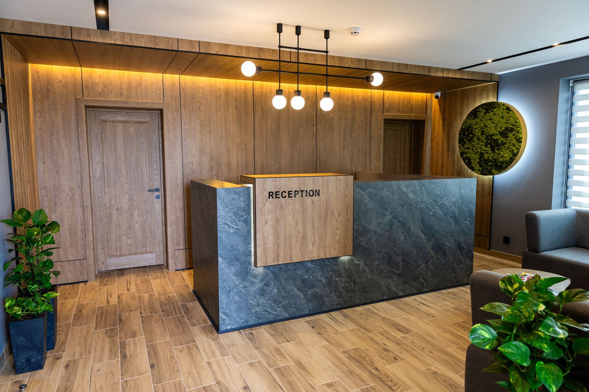 Modern office reception area with wood-paneled wall, blue stone desk, pendant lights, and potted plants