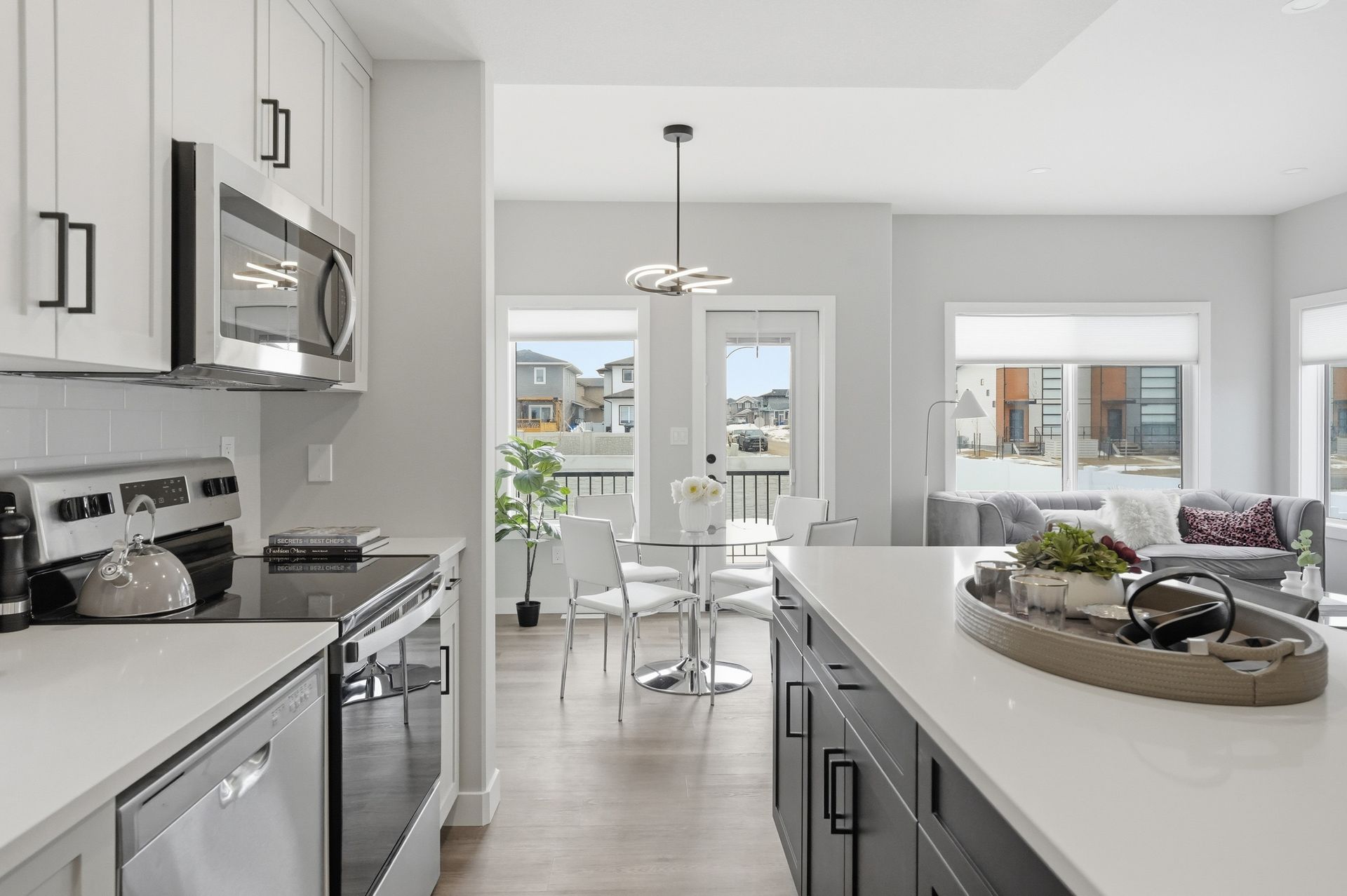 Modern white kitchen with island, stainless appliances, and dining area by bright windows