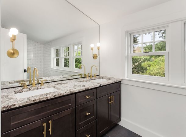 Modern bathroom vanity with granite countertop, dark wood cabinets, gold fixtures, and a large mirror