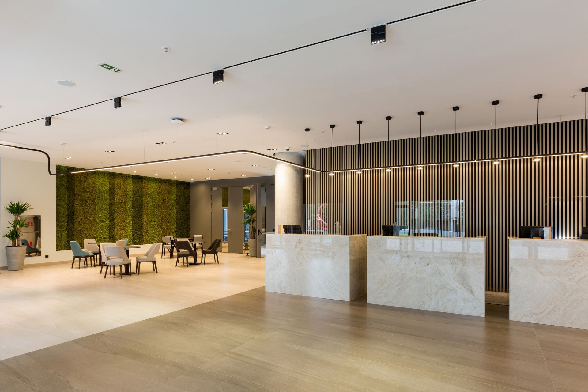 Modern office lobby with marble reception desk, wood flooring, lounge seating, and vertical green wall