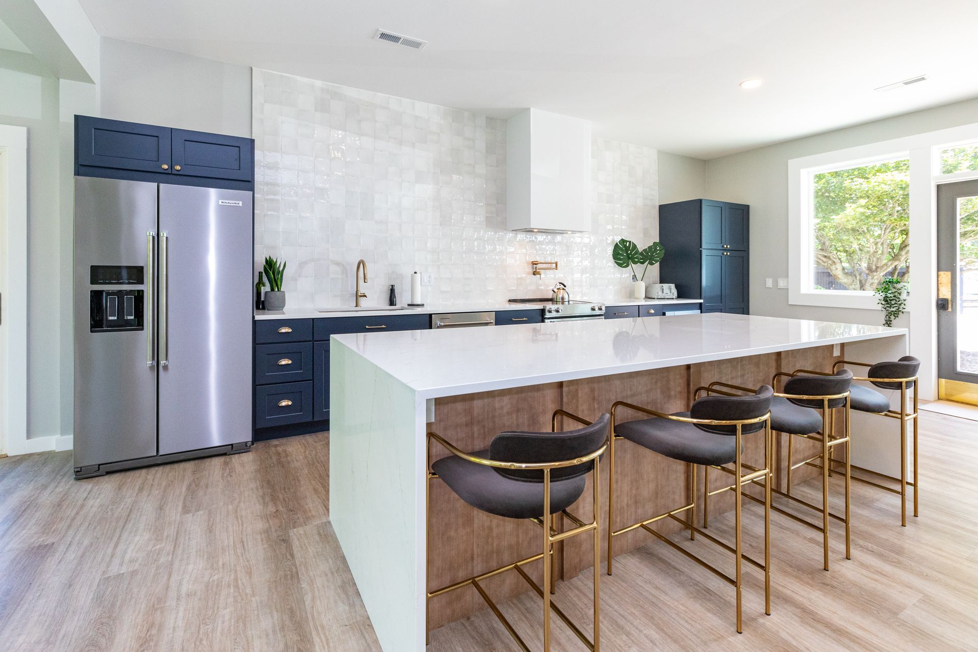 Modern kitchen with stainless steel appliances, dark blue cabinets, and a white island with bar stools.