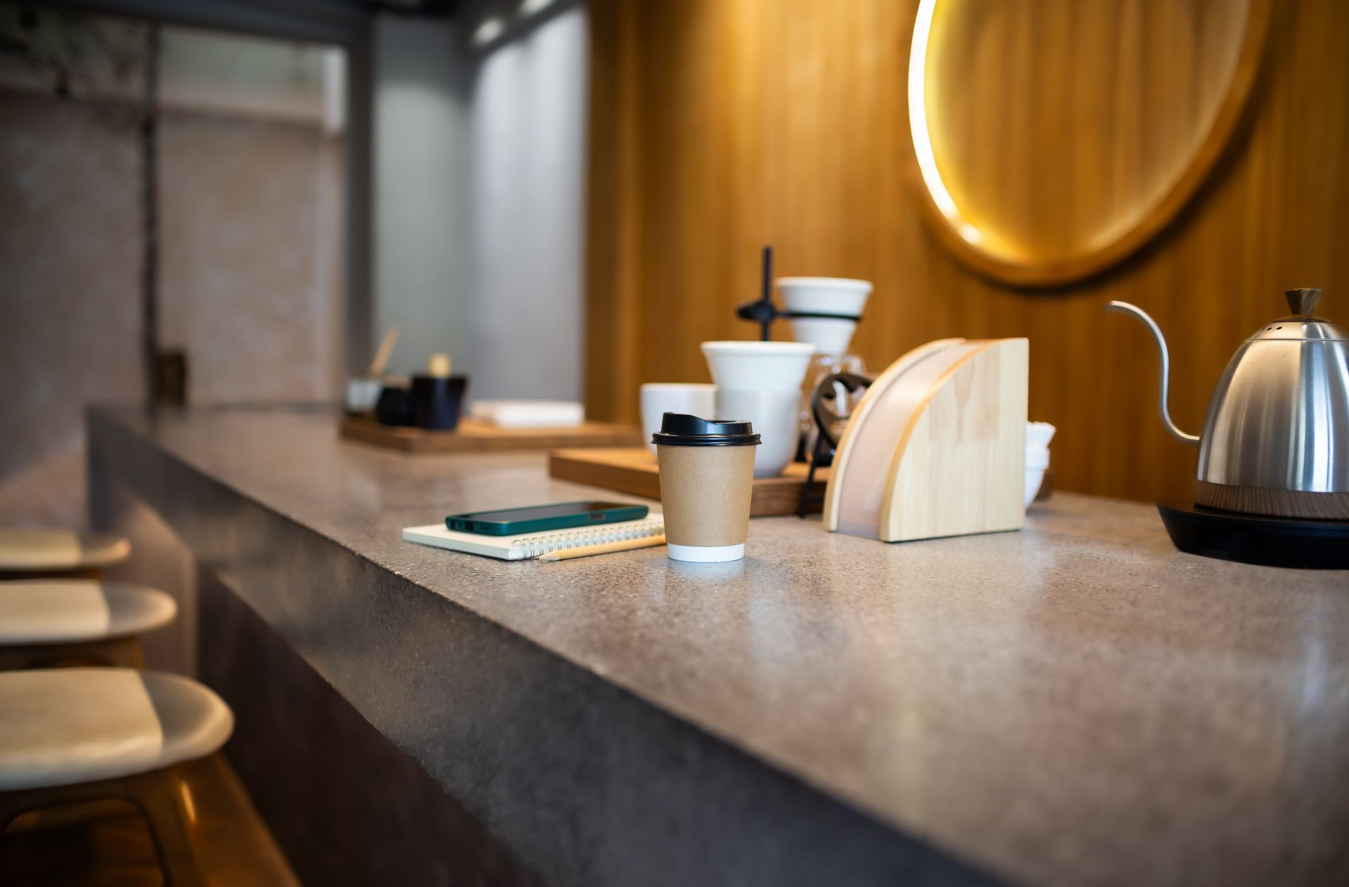 Coffee shop counter with cups, napkins, and a stainless-steel kettle on a wooden bar