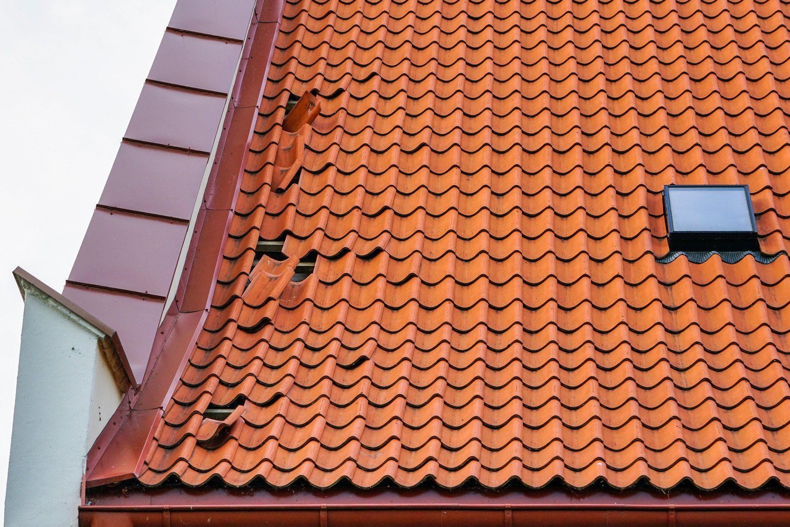 Red tile roof with a small skylight and metal flashing. Some tiles are missing.