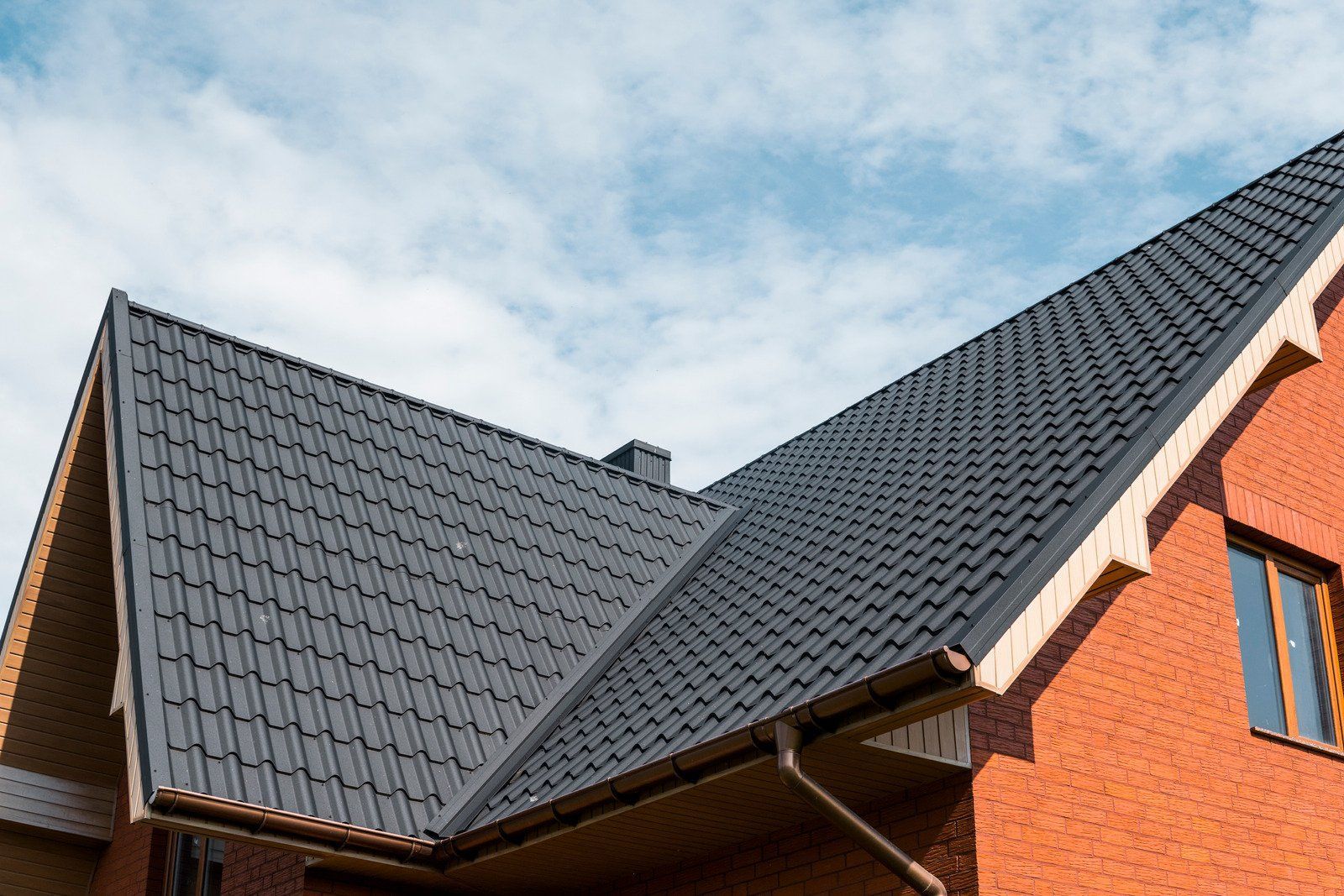 Red brick house with a black tiled roof against a partly cloudy sky.