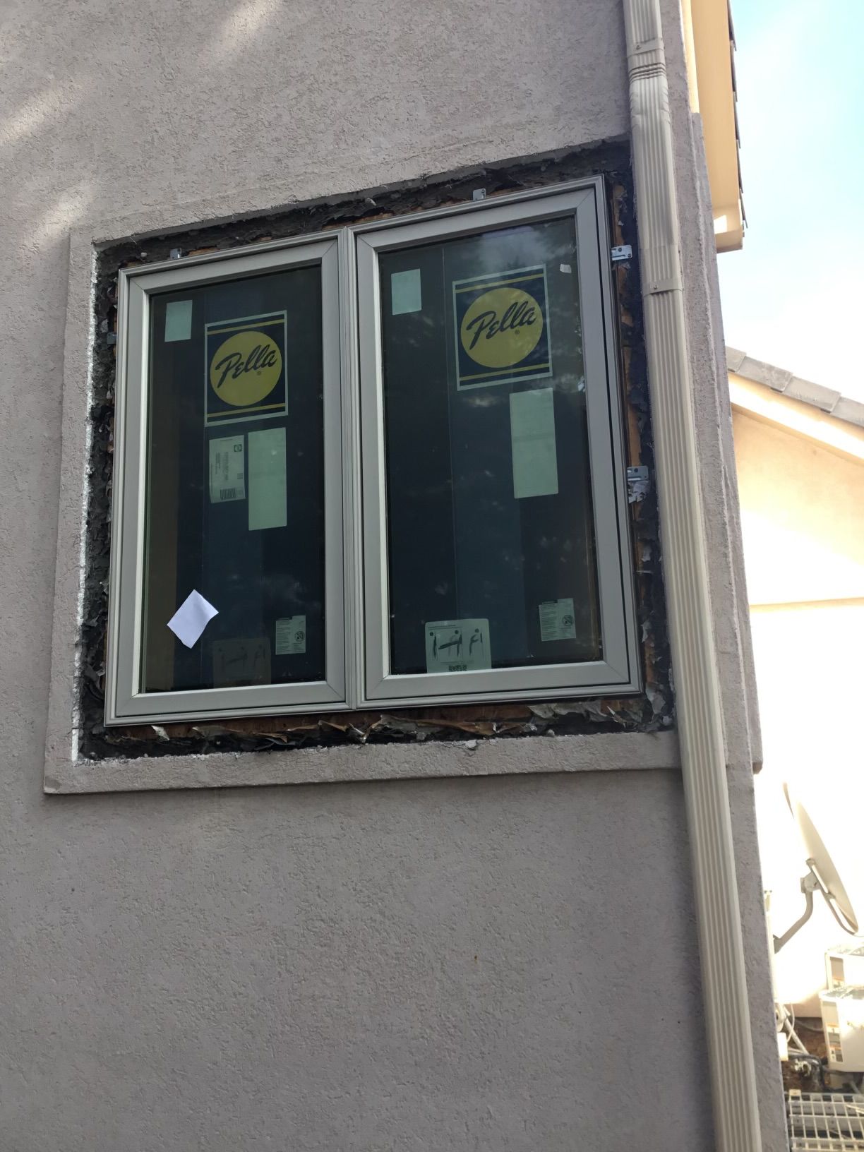 Window installation on a stucco wall; the new window has protective yellow stickers and is surrounded by dark sealant.