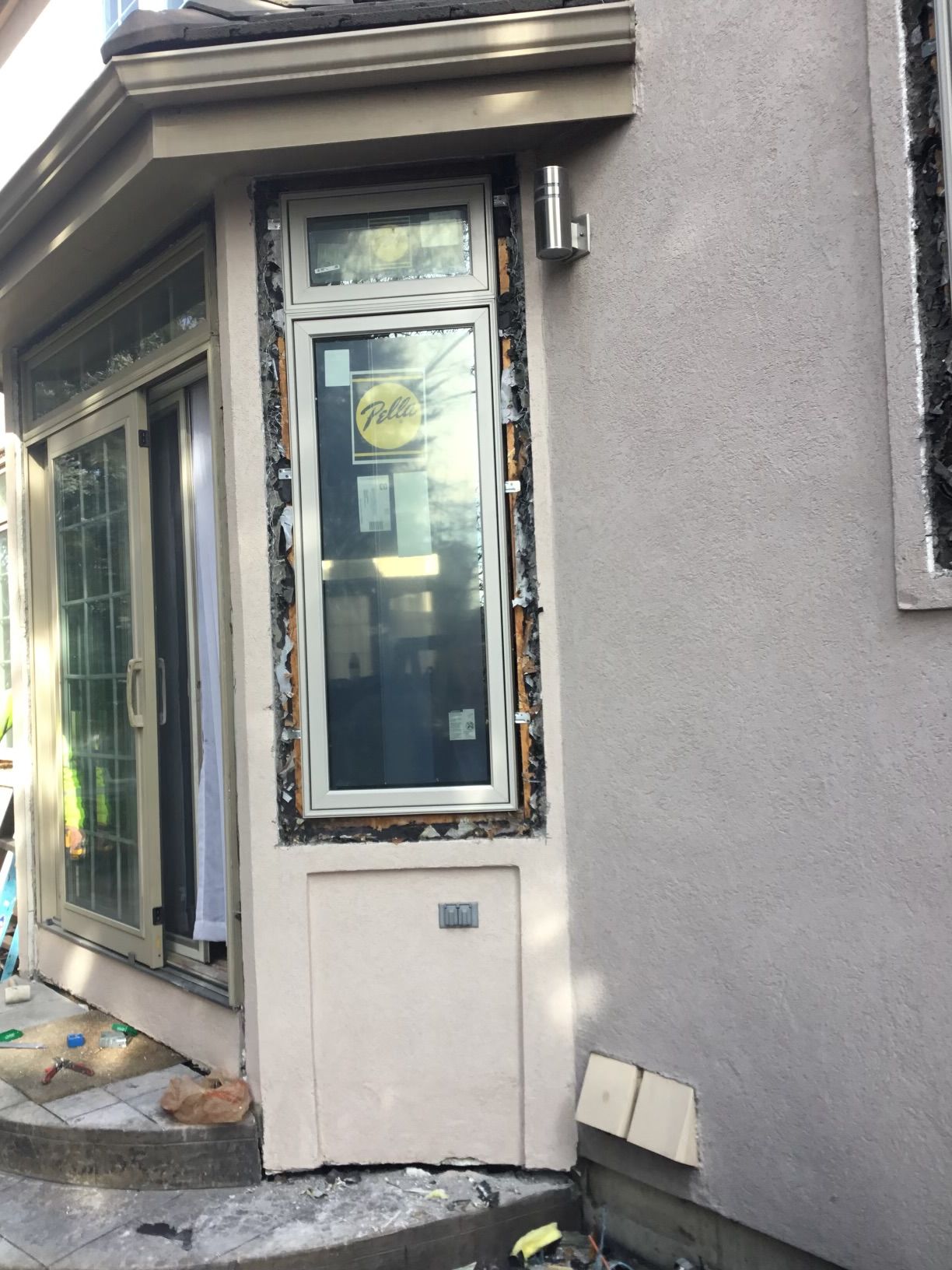 Exterior view of a house with a new window installed, showing unfinished framing and stucco wall.