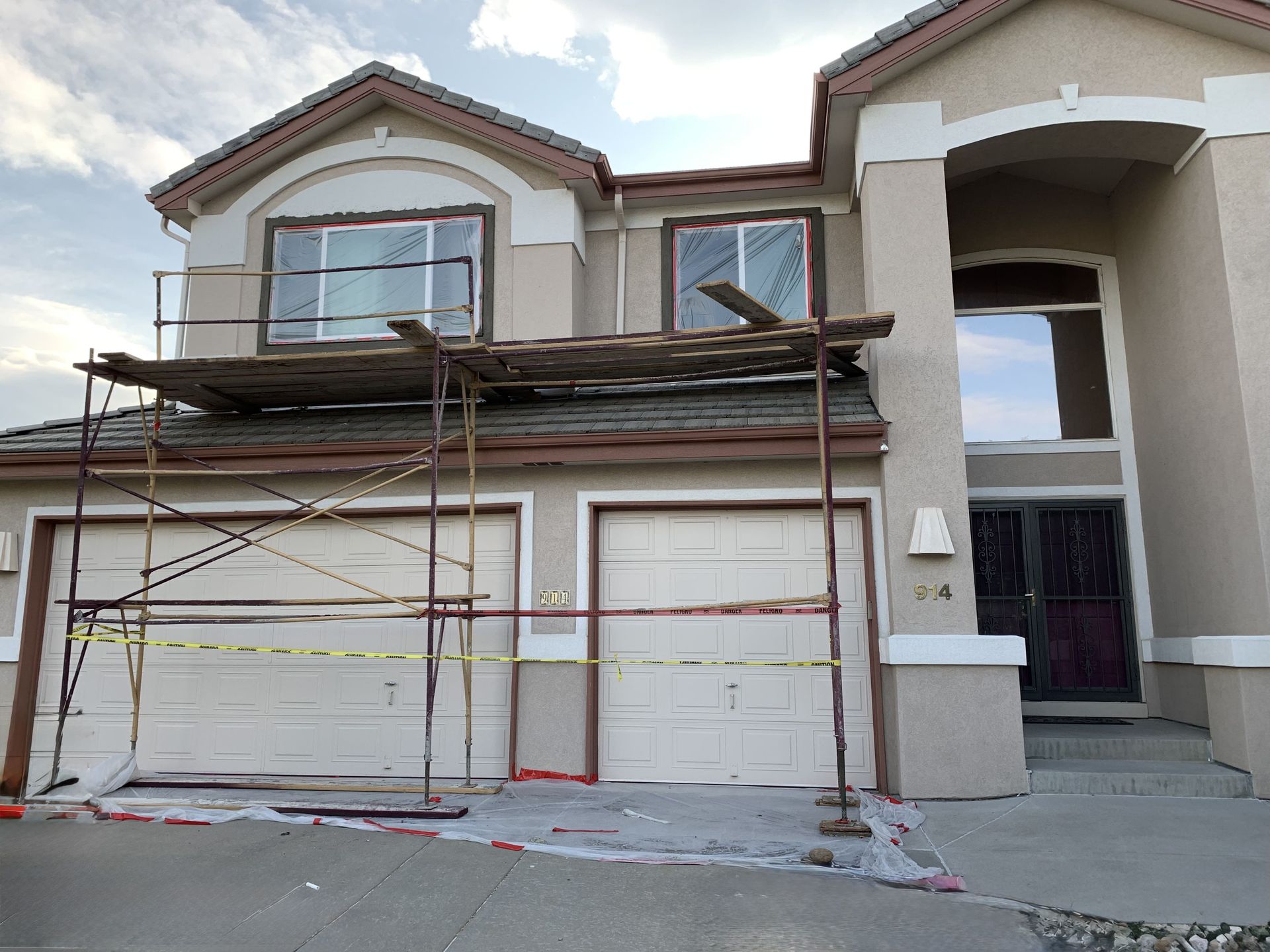 House exterior undergoing renovations. Scaffolding set up in front of the garage.  Exterior painted tan with brown trim.