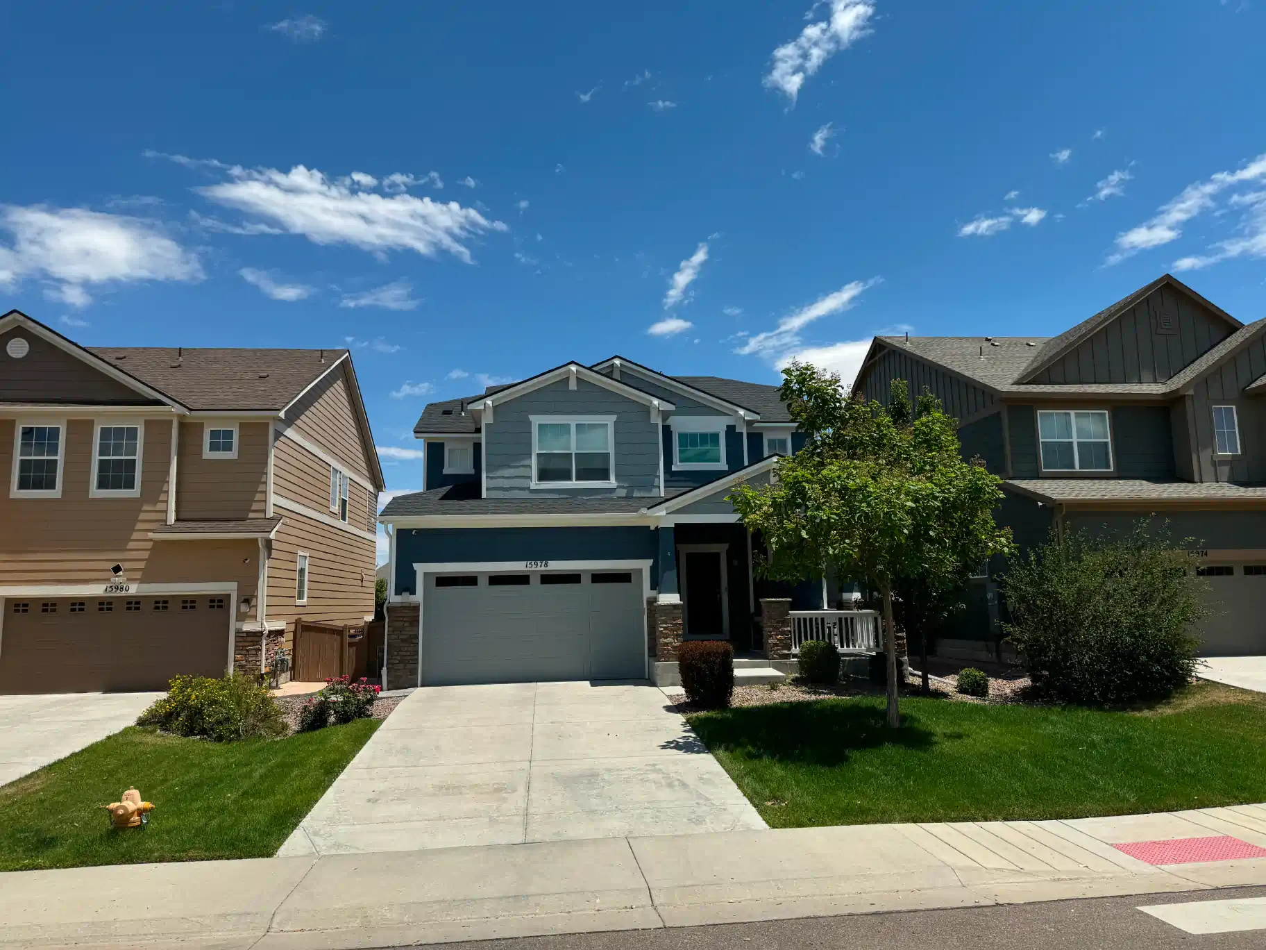 Suburban homes with blue, tan, and brown siding under a bright blue