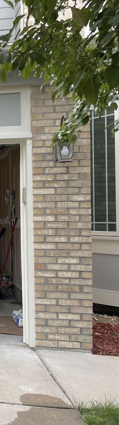 A brick pillar supports a building entrance with a light fixture.  A tree branch partially obscures the top.