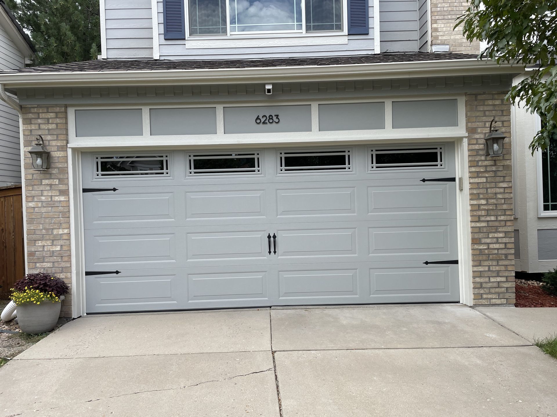 Gray garage door on a house with stone accents. Door has windows and decorative hardware, address 