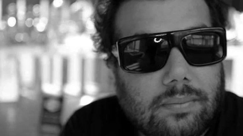 Um homem com barba e óculos escuros em uma foto em preto e branco.