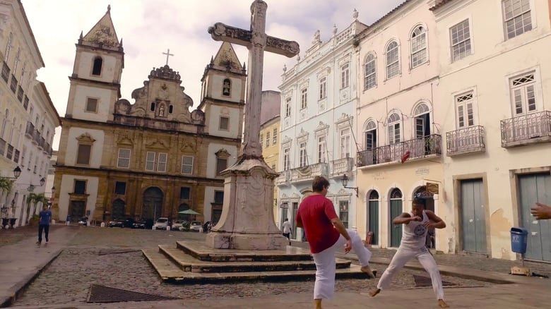 Duas pessoas estão diante de uma cruz em uma praça da cidade.