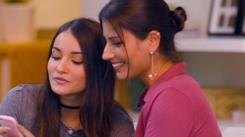 Duas mulheres estão sentadas uma ao lado da outra olhando para um celular.