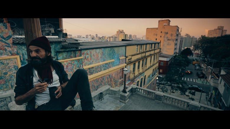 Um homem barbudo está sentado no telhado de um prédio.