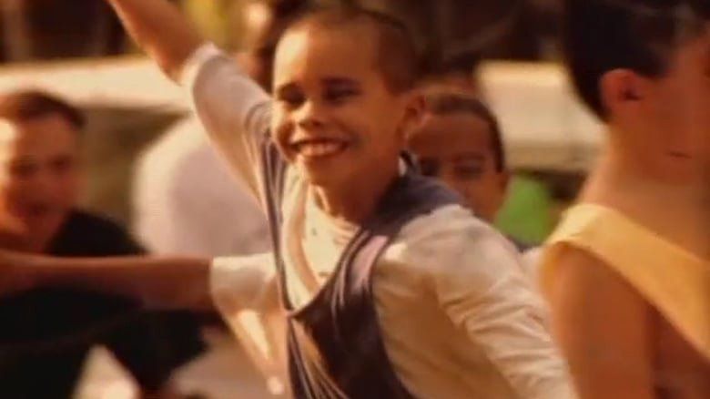 Um menino de camisa azul está sorrindo com o braço no ar