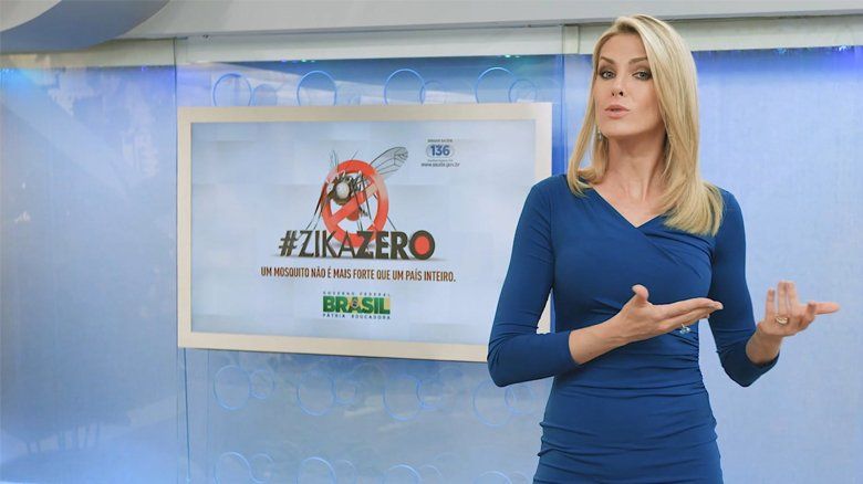 Uma mulher de vestido azul está parada em frente a uma tela.