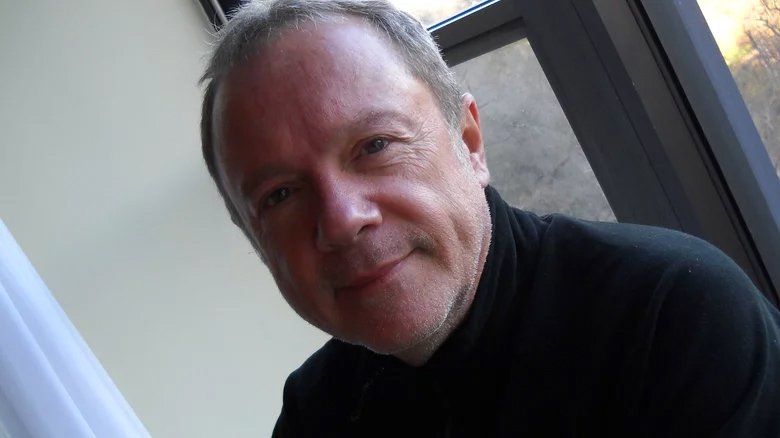 Um homem de gola alta preta está sorrindo e olhando para a câmera.