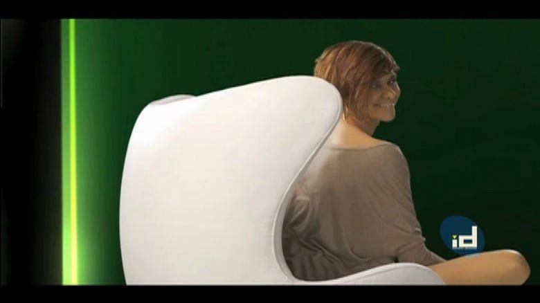 Uma mulher está sentada em uma cadeira branca com fundo verde