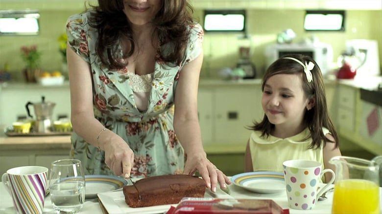 Uma mulher e uma menina estão sentadas à mesa cortando um pedaço de bolo.